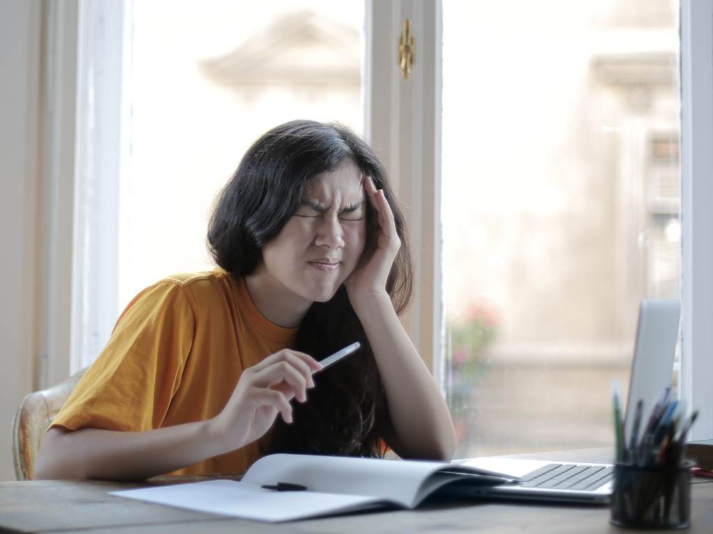 woman squinting in pain from headache while reading